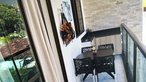 Een balkon met een zwarte opklapstoel, een tafeltje met stoelen en uitzicht op het omliggende landschap.