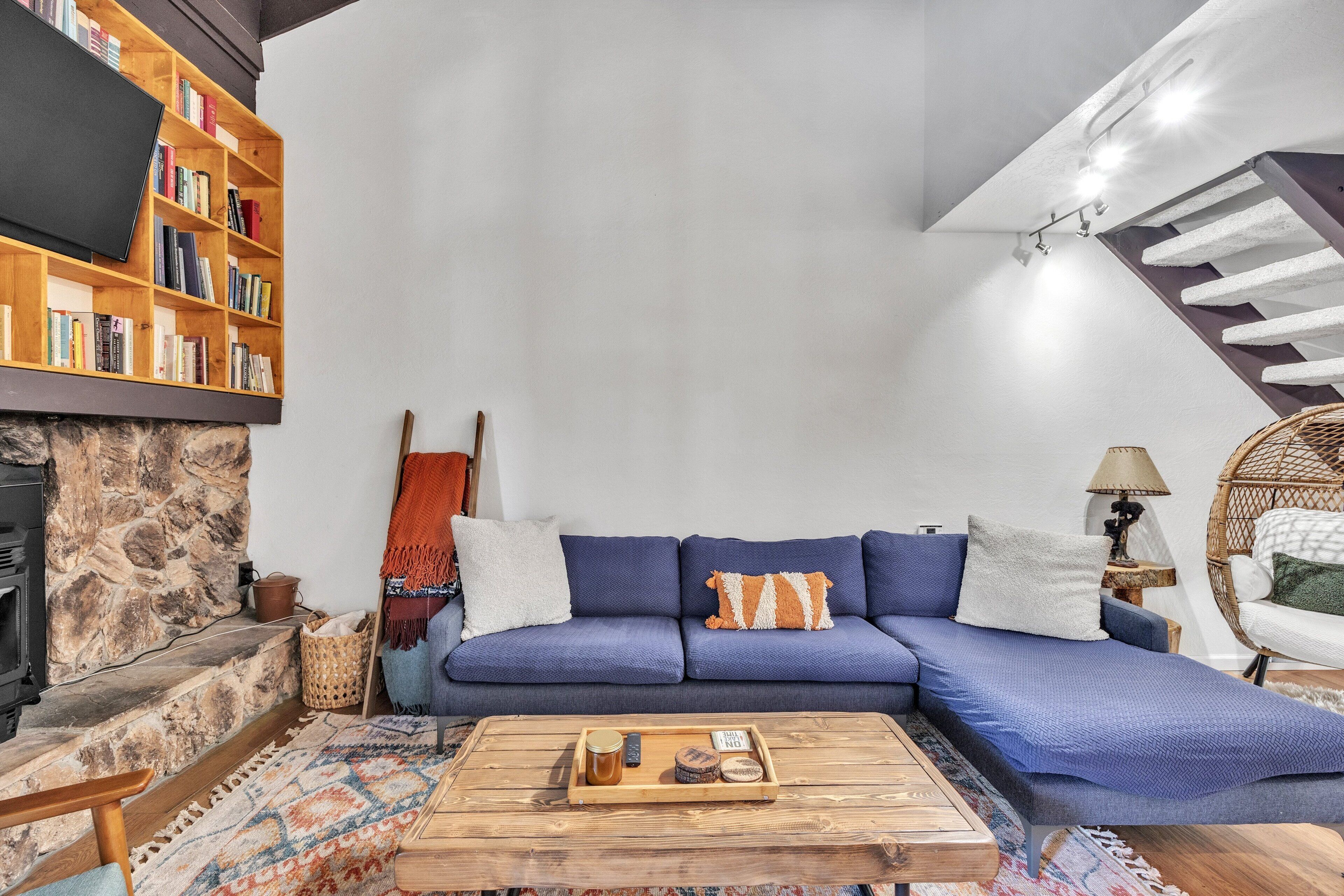 A cozy living room with a blue sofa, a wooden coffee table, a bookshelf, and a stone fireplace.