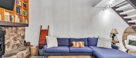 A cozy living room with a blue sofa, a wooden coffee table, a bookshelf, and a stone fireplace.
