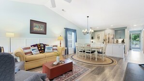A modern living room with a sofa, a coffee table, and a dining area with chairs and a table. - 65d Isle Awhile 3 Bedroom Condo (Pawleys Island)