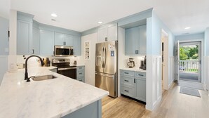 A modern kitchen with light blue cabinets, stainless steel appliances, and a marble countertop. - 65d Isle Awhile 3 Bedroom Condo (Pawleys Island)