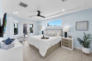 A modern bedroom with a large bed, bedside tables, a ceiling fan, and a window with a view.