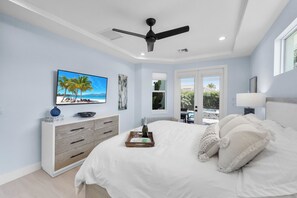 A bedroom with a bed, a ceiling fan, a TV, a dresser, and a window with a view of the outdoors. - 2023 Custom Built Home | Heated Pool & Hot Tub (Marco Island)