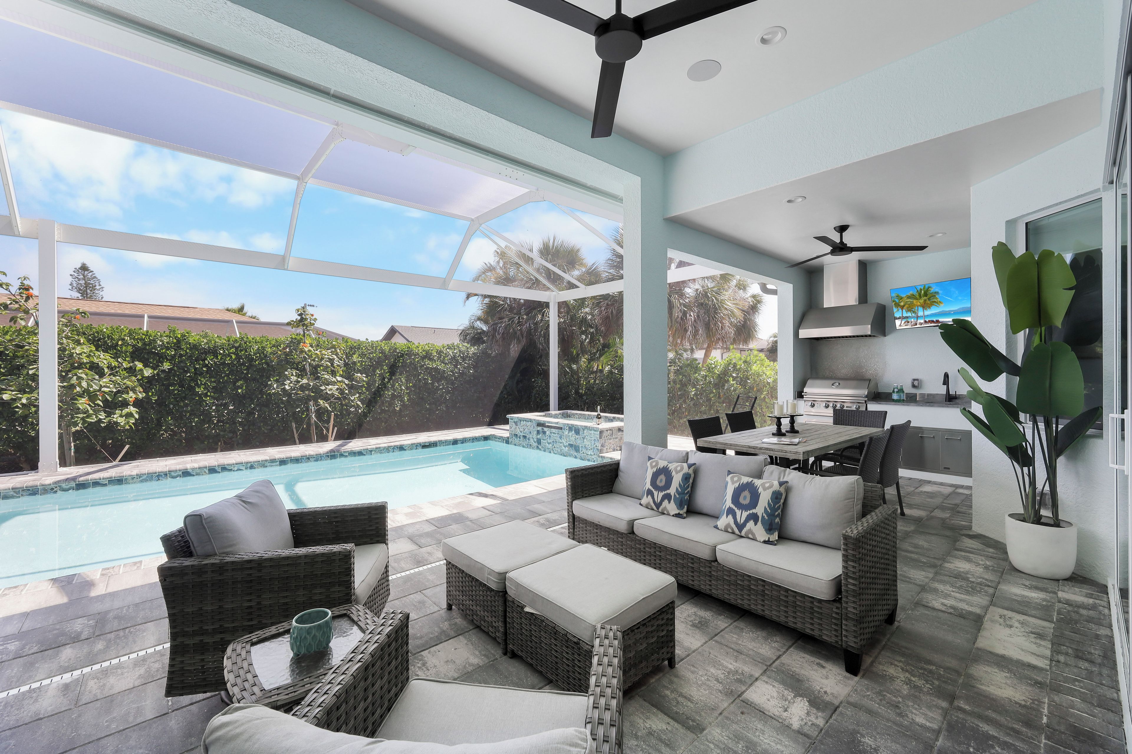 A modern outdoor living area with a pool, wicker furniture, and a kitchen area.