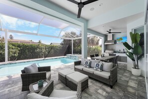 A modern outdoor living area with a pool, wicker furniture, and a kitchen area. - 2023 Custom Built Home | Heated Pool & Hot Tub (Marco Island)