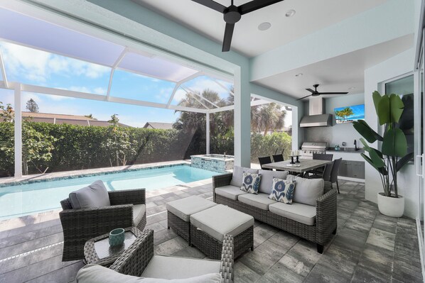 A modern outdoor living area with a pool, wicker furniture, and a kitchen area.