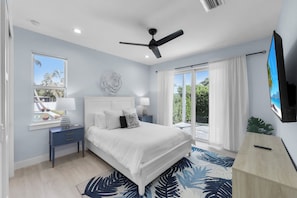 A bedroom with a bed, nightstands, a ceiling fan, a TV, and a view of the outdoors.
