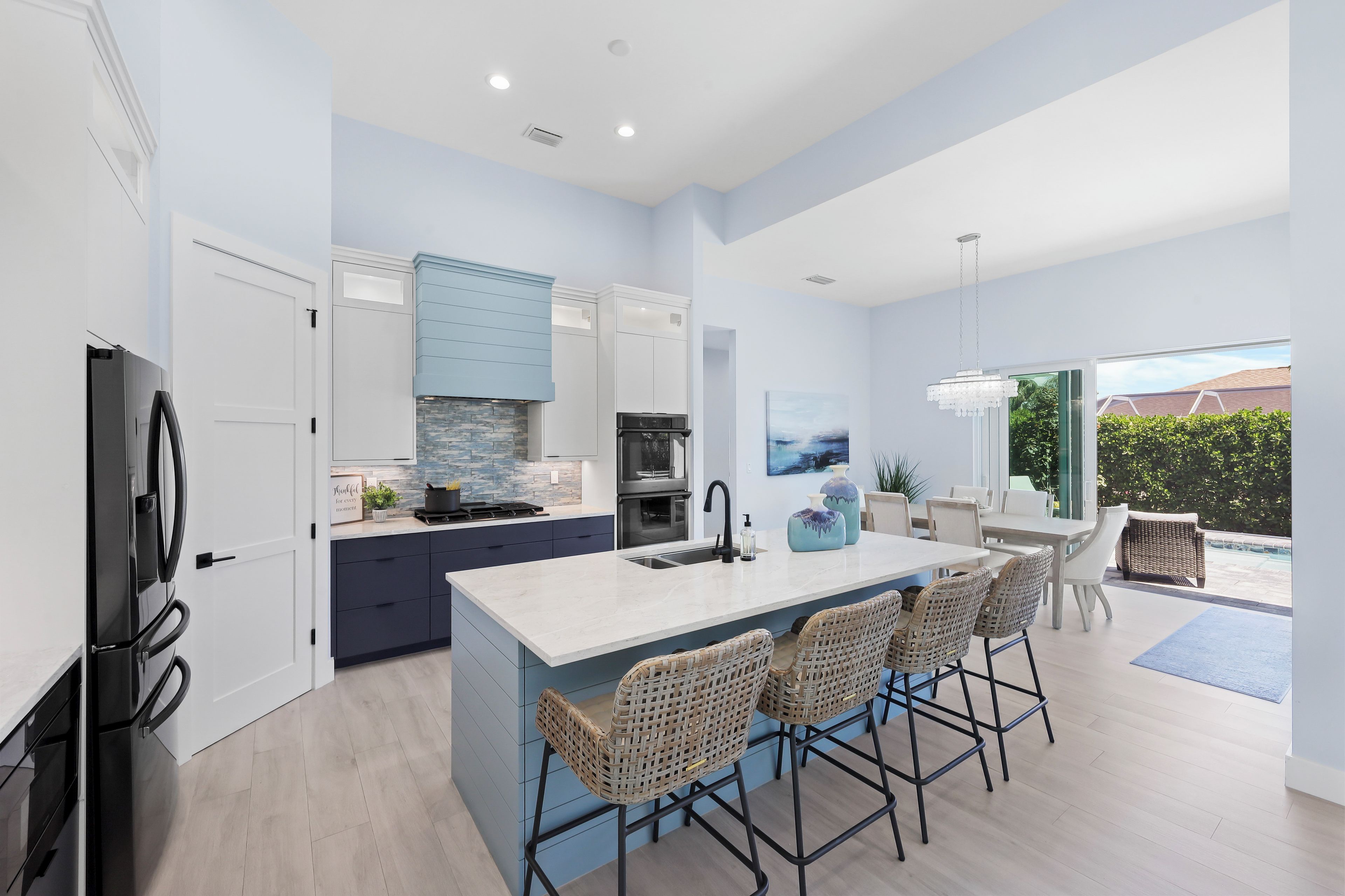 A modern kitchen with a large island, bar stools, and a dining area with a view of the outdoors.