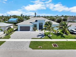 A modern two-story house with a garage, surrounded by well-maintained lawns and palm trees. - 2023 Custom Built Home | Heated Pool & Hot Tub (Marco Island)