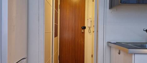 Un couloir étroit avec un plancher en bois, des murs blancs et une porte au fond.