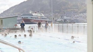 Une piscine avec des personnes dans l’eau et un grand navire en arrière-plan.
