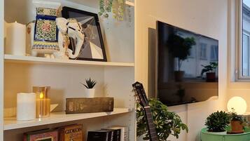 Un salon avec une bibliothèque, une guitare, un téléviseur et une petite table sur laquelle est posée une plante.