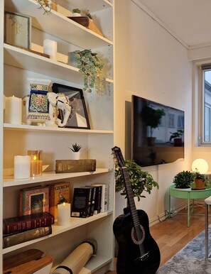 Ein Wohnzimmer mit Bücherregal, Gitarre, Fernseher und einem kleinen Tisch mit Pflanze.