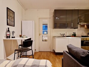 A compact living space with a kitchenette, a dining area with a chair, a sofa, and a door leading to a blue room. - Cozy condo near Bryggen, Full kitchen, Elevator (Bergen)
