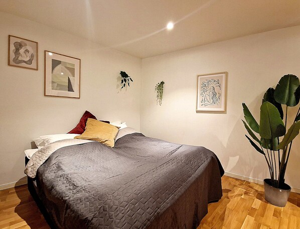 Un dormitorio con cama, almohadas, una planta grande en maceta y obras de arte enmarcadas en las paredes.