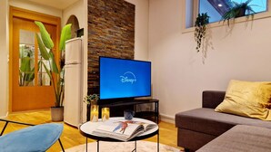 Un salon moderne doté d’un téléviseur à écran plat affichant le logo de Disney+, d’un canapé gris, d’un fauteuil bleu et d’une petite table sur laquelle sont posés des magazines.