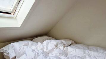 Uma cama de solteiro num quarto com teto inclinado e claraboia.