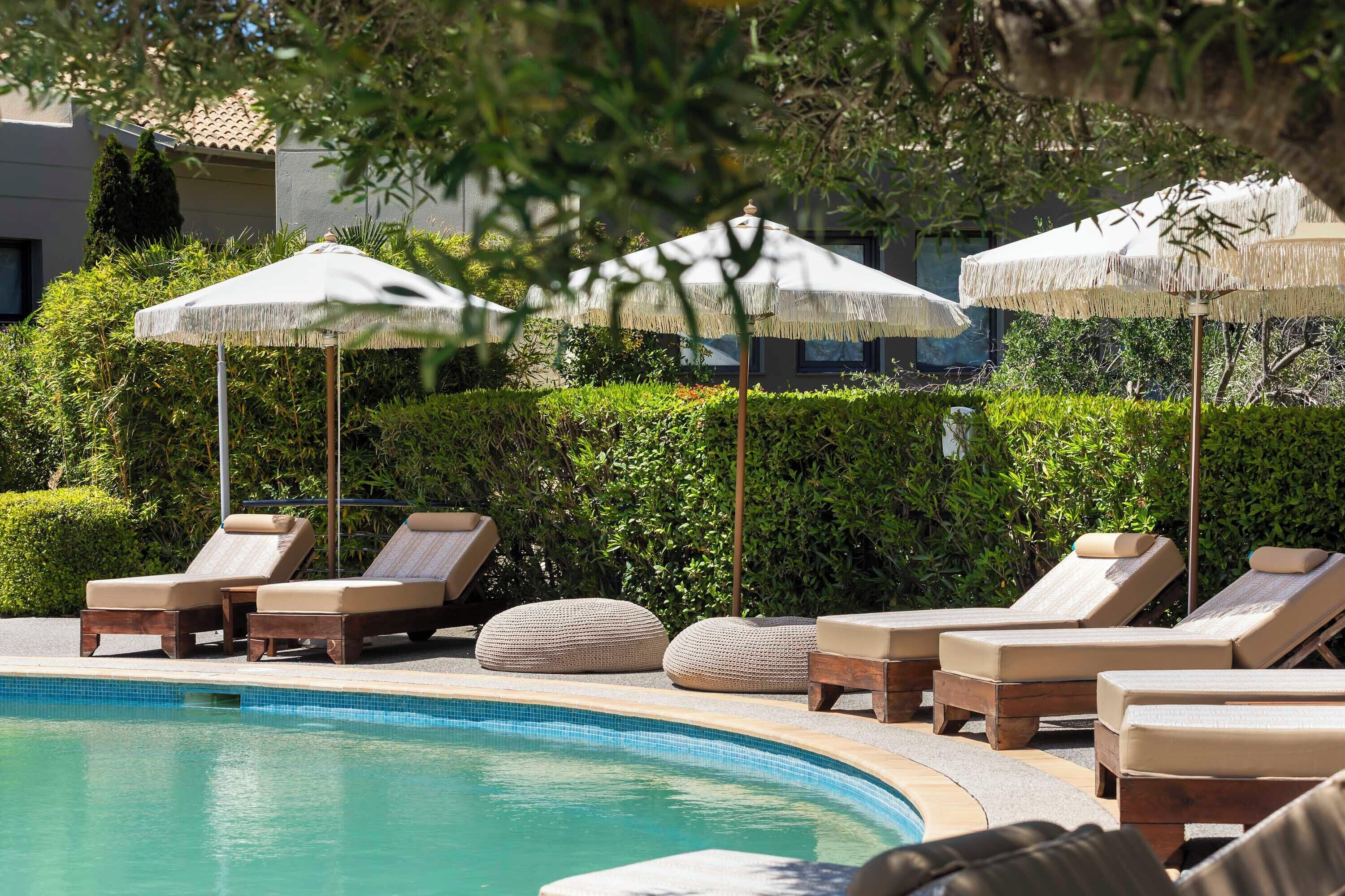 A poolside area with lounge chairs and umbrellas, surrounded by greenery.