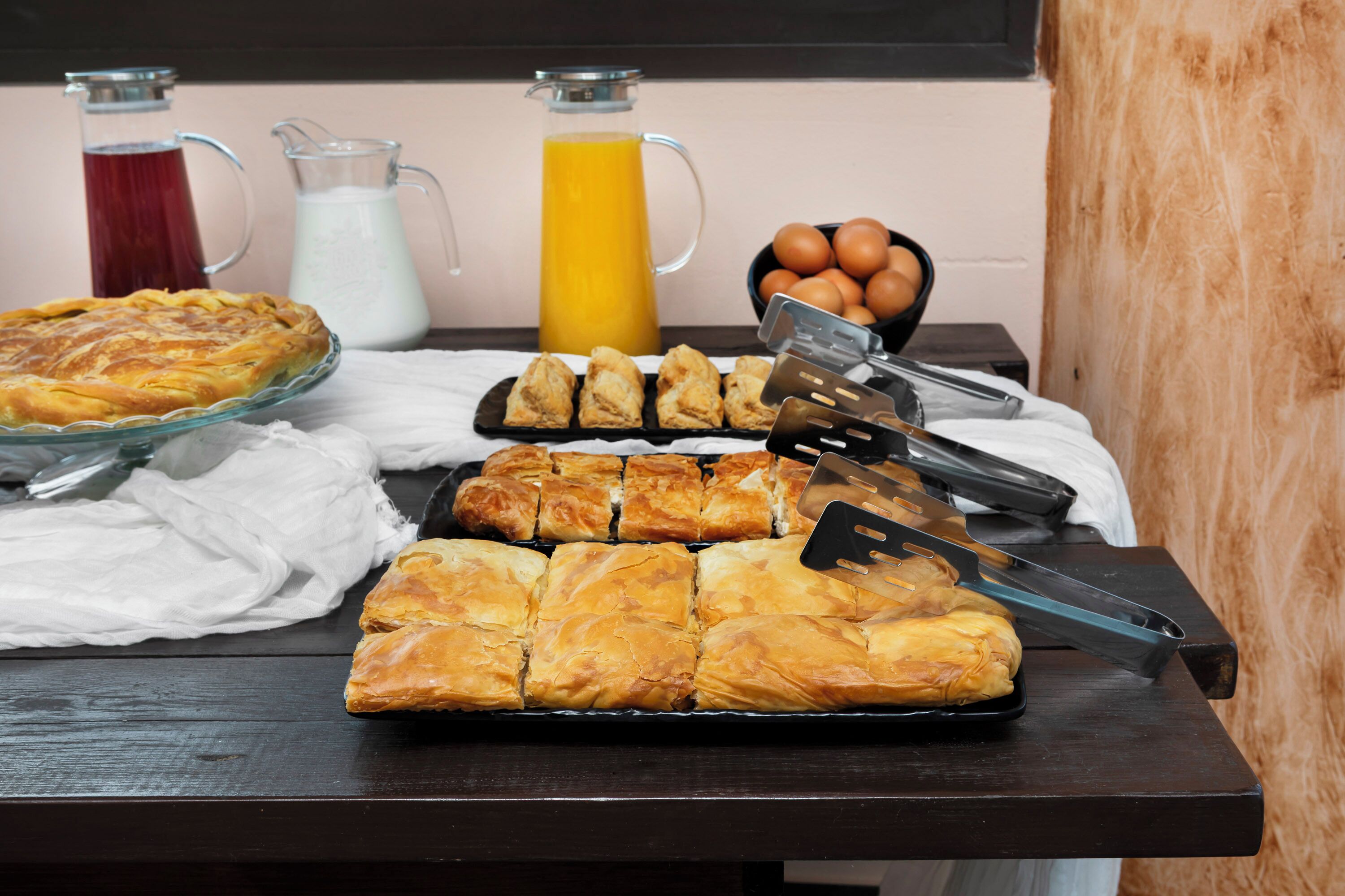Una mesa de desayuno con pasteles, un pastel, una jarra de leche y una jarra de jugo de naranja, junto con un bol de huevos.