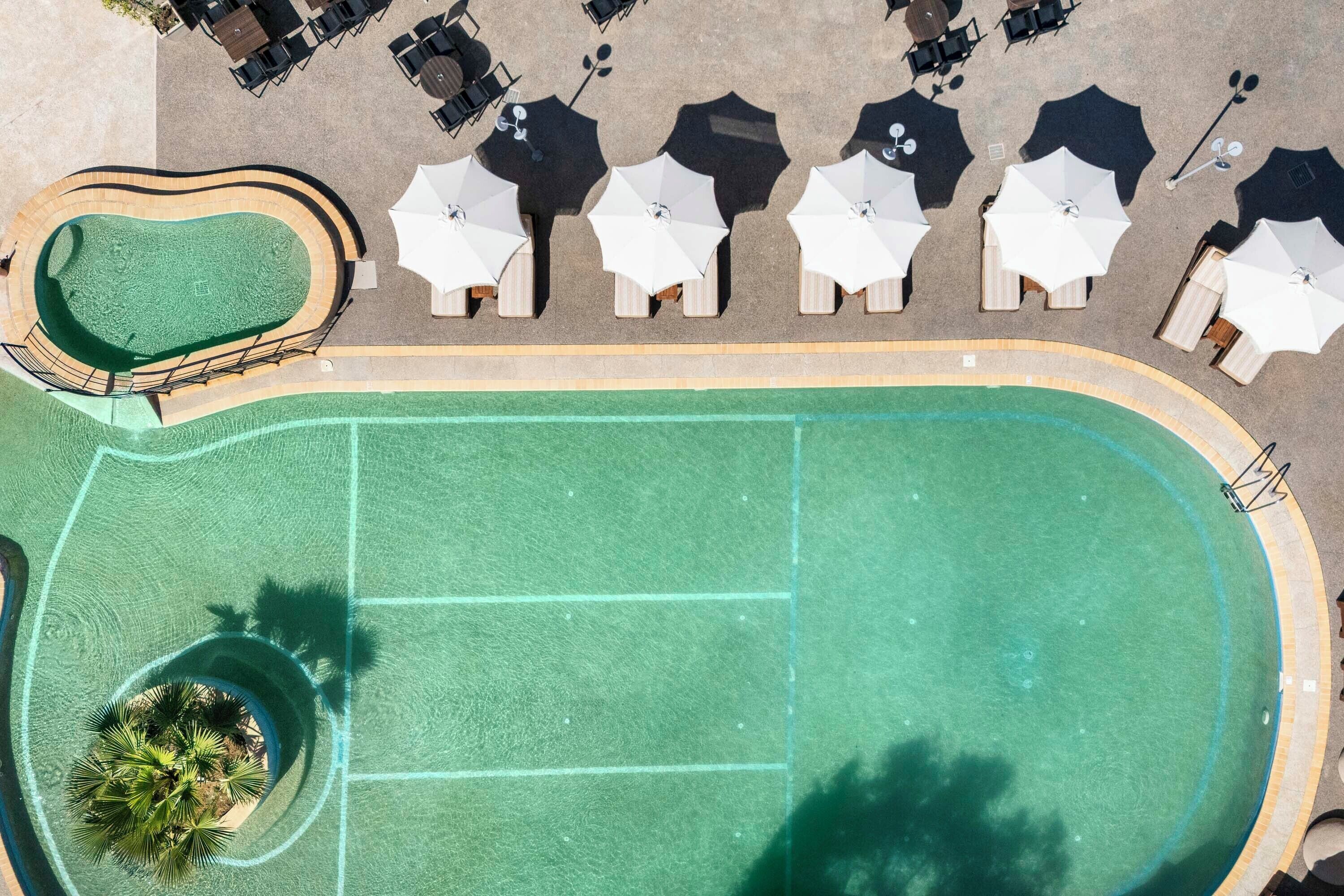 An aerial view of a swimming pool with a surrounding deck area, including sun loungers and umbrellas.