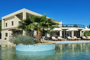 Um hotel moderno com piscina, espreguiçadeiras e uma palmeira.
