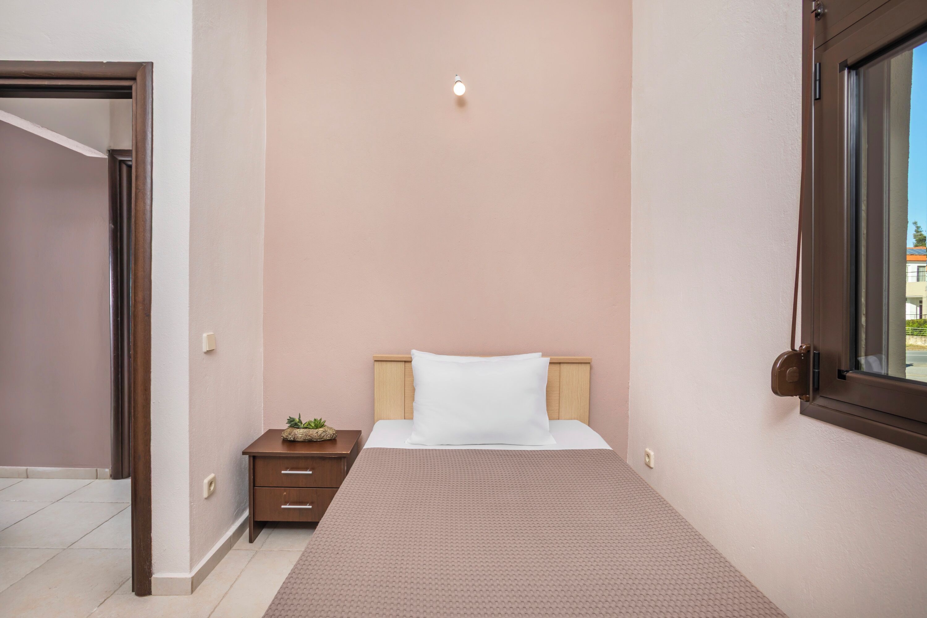 A bedroom with a bed, a nightstand, a small plant, and a window.