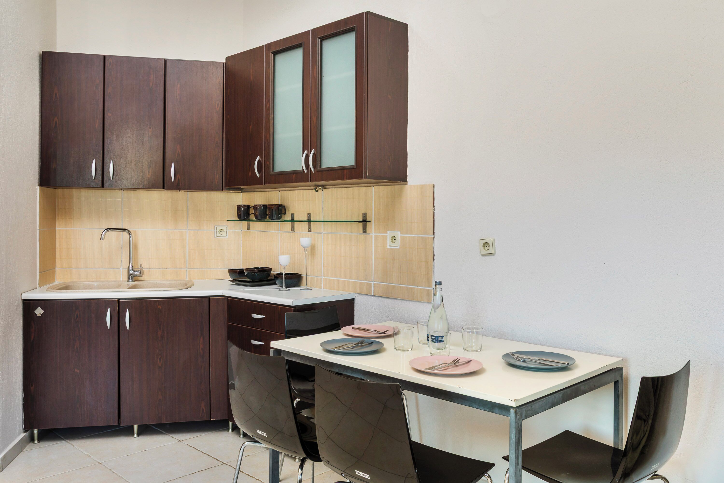 A compact kitchen with dark wooden cabinets, a white countertop, and a dining area with a table and chairs.