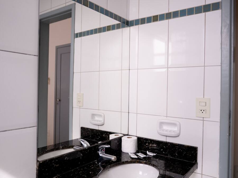 A bathroom with white tiled walls, a black granite sink, and a mirror above it.
