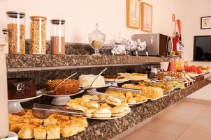 Buffet com diversos alimentos e recipientes, incluindo bolos, doces e cereais.