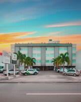 Um hotel com estacionamento, vários carros e palmeiras na frente.