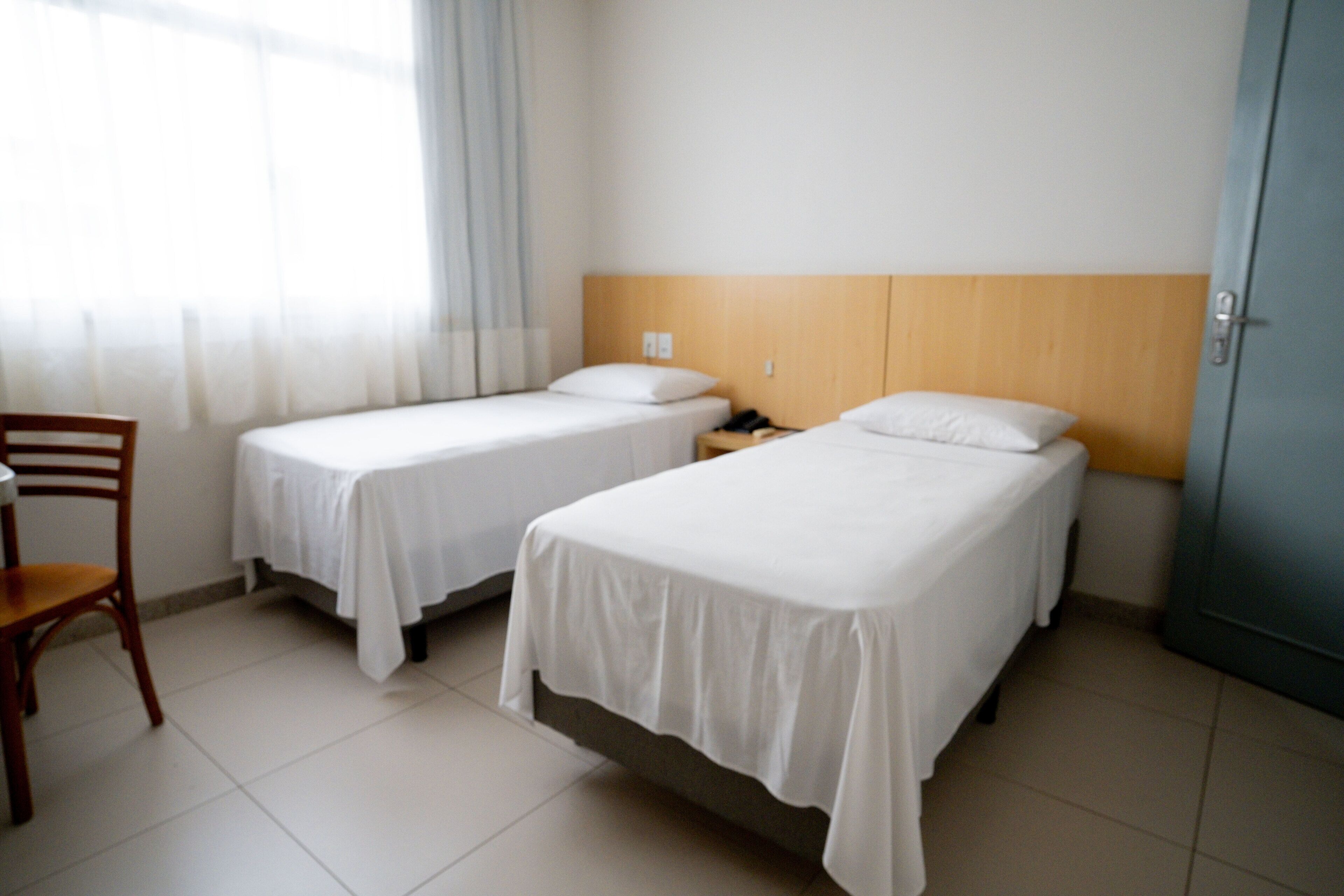 A hotel room with two single beds, a wooden headboard, a chair, and a nightstand.
