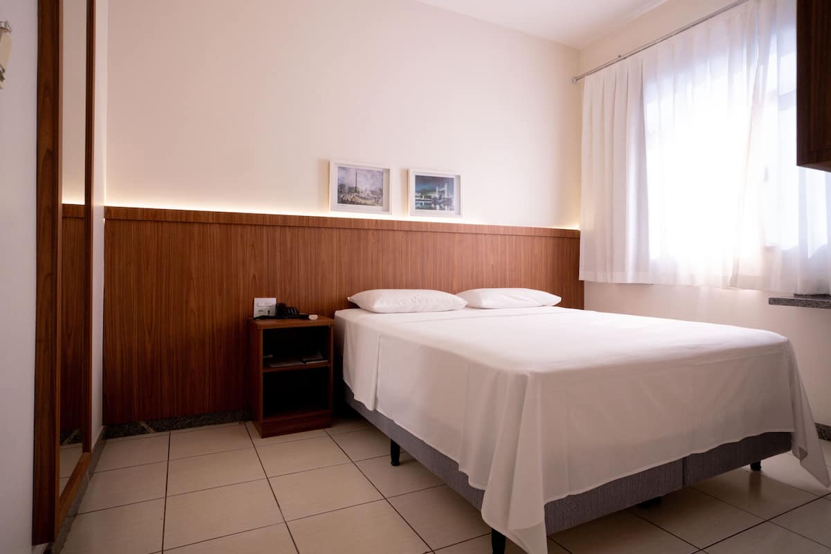 A hotel room with a wooden headboard, a bed with white linens, a nightstand, and two framed pictures on the wall.