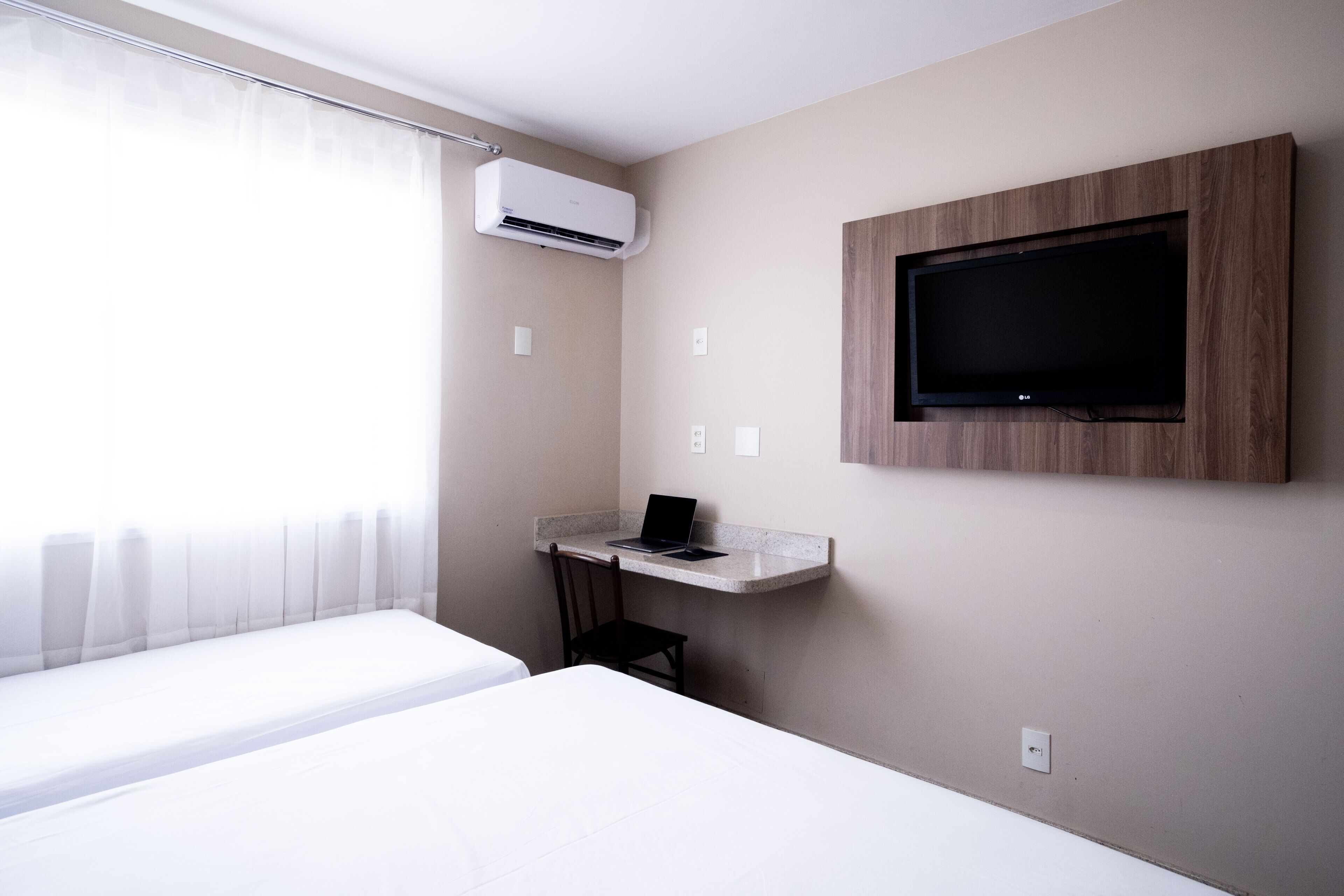 Habitación de hotel con cama, escritorio, computadora portátil, aire acondicionado y televisión montada.