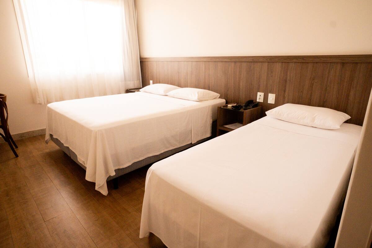 A hotel room with two single beds, a wooden headboard, a nightstand with a phone, and a window with curtains.