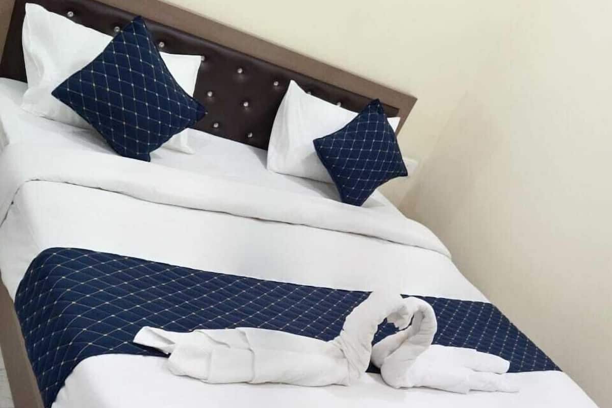 A neatly made bed with white and blue bedding, a brown headboard, and a pair of white towels arranged on the bed.