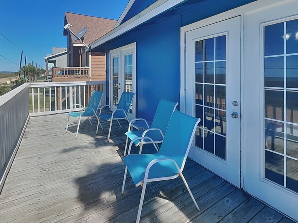 A wooden deck with blue chairs and a glass door.