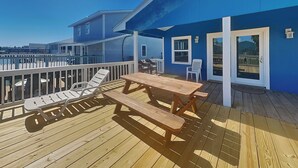 Una terraza de madera con una mesa de picnic y sillas reclinables, con vistas a un cuerpo de agua.