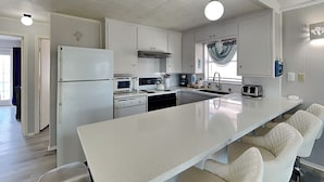 Una cocina moderna con armarios blancos, una isla grande con taburetes de bar, electrodomésticos de acero inoxidable y un ventanal con vistas.