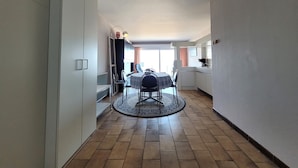 A narrow hallway with a dining area featuring a round table and chairs, a kitchen area with a sink and countertop, and a door leading to another room.