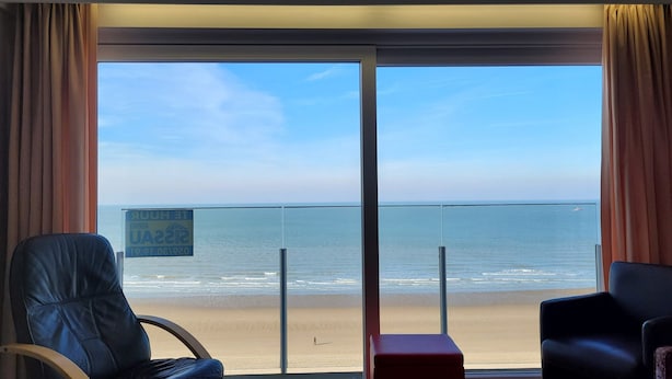 A room with a large sliding glass door leading to a balcony with a view of the beach.