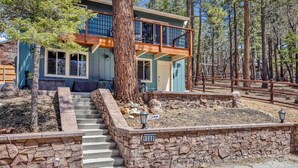 A two-story house with a stone staircase leading to a wooden deck, surrounded by trees.