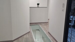 Un couloir doté d’un plancher en verre, de murs blancs et d’une petite plante posée sur une étagère.