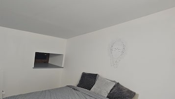 A modern bedroom with a bed, a small window, and a wall decoration.