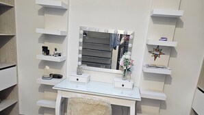 Une coiffeuse avec un miroir, des étagères et un petit tabouret moelleux.