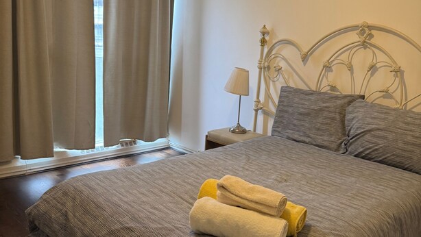 A neatly made bed with a patterned bedspread, a metal headboard, and a nightstand with a lamp. - Calm and Cosy Apartment in Central London (London)
