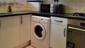 A compact kitchen with white cabinets, a washing machine, a microwave, and a stove. - Calm and Cosy Apartment in Central London (London)