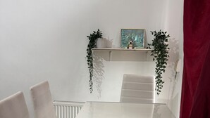 A white dining table with four chairs, a radiator, a shelf with plants and a picture, and a red curtain. - Calm and Cosy Apartment in Central London (London)
