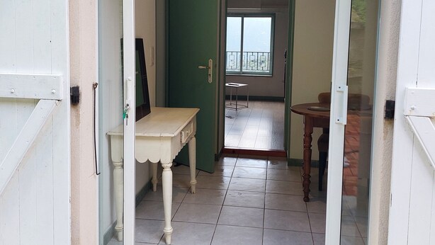 Une pièce avec une table blanche et une porte verte, un balcon avec une table, et un sol carrelé.