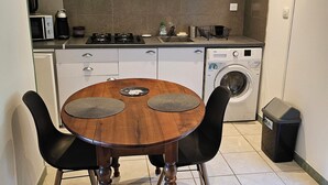 Une cuisine compacte comprenant une table à manger, des chaises, un four à micro-ondes, une machine à café, un lave-linge et une poubelle.