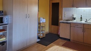 Eine kleine Küche mit Holzschränken, einer Mikrowelle, einer Kaffeemaschine und einem Spülbecken.